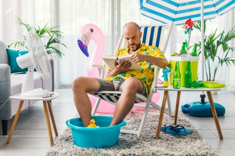 3 Signs It’s Time for a New AC. Man in his living room sitting on a deckchair with his feet in a mini pool reading a book.