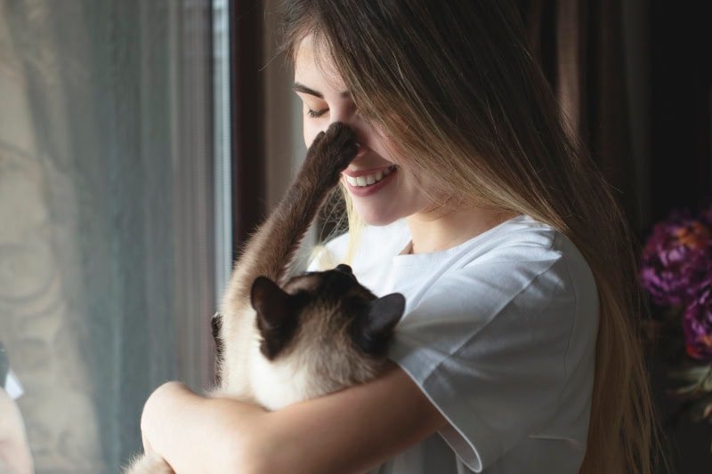 young woman hugging her cat in front of the window.