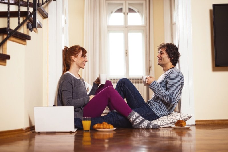 How to Determine Heat Pump Efficiency. Couple sitting on the floor drinking out of mugs and eating breakfast.